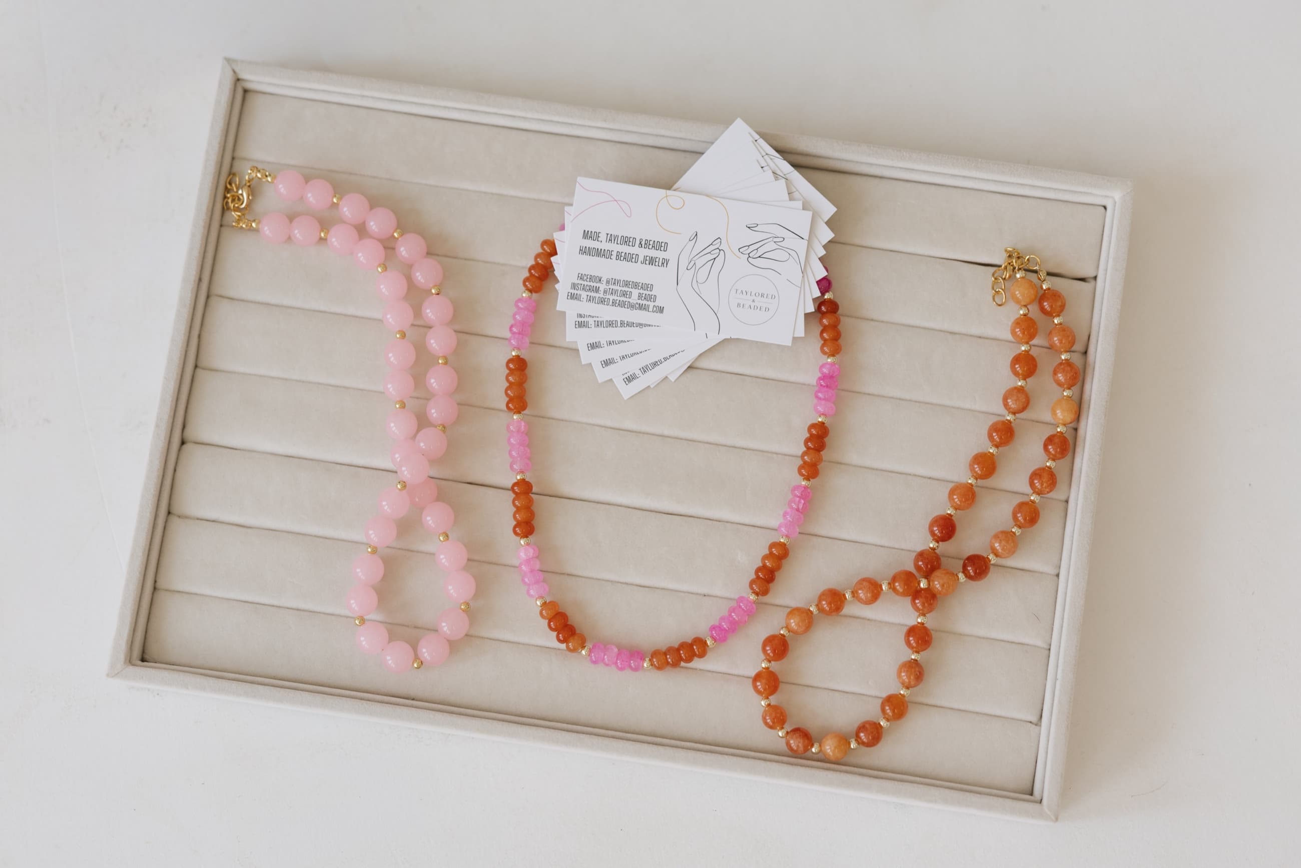 Pink and orange beaded necklaces arranged on a linen jewelry tray with Taylored & Beaded cards